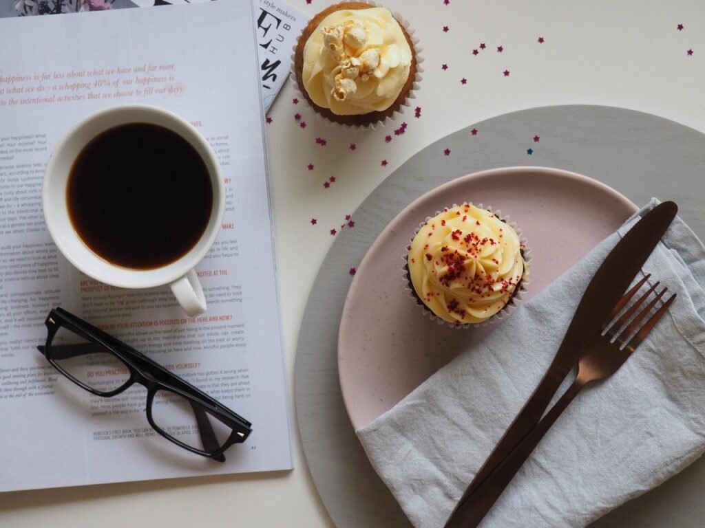 coffee, cup, drink, breakfast, food, chocolate, sweet, table, sugar, espresso, spoon, plate, tea, hot, mug, saucer, glasses, desktop, table top, cupcake, cake, coffee cup, icing, dessert, tea cup, table wear, magazine, read, cafe, caffeine, cappuccino, white, black, beverage, morning